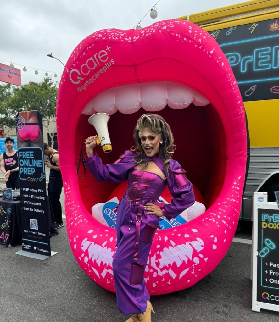 Drag Queen Jo Lopez standing in front of an inflatable mouth and the Grindr Bus