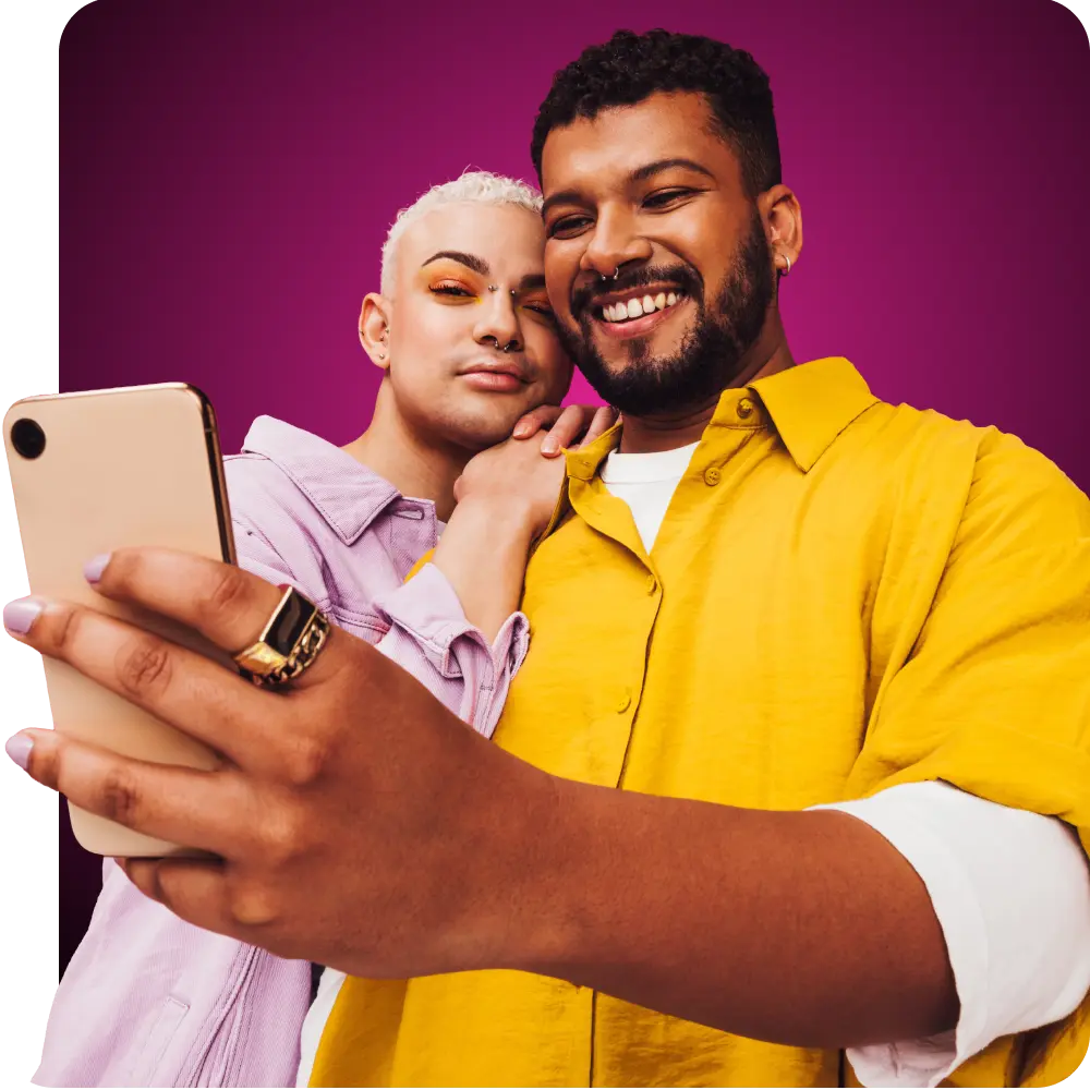 Una pareja gay con ropa brillante sonríe mientras mira su teléfono